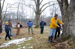 Creek Iverson, manager of the Brook Farm Project, New Paltz, NY, explains to a group of people volunteering for a day of maple sugaring prep work, that in order to tap a sugar maple tree in the best spot possible, one should find a spot where the tree is the warmest, typically where the sun hits the tree the most, which would be located on the south side of the tree’s trunk. Photo by Dawna M. Cservak.