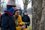 Ben Gilman, a young volunteer at the Maple Sugaring Prep Work party and potluck (right), looks on with serious determination as he watches Creek Iverson, manager of the Brook Farm Project, New Paltz, NY, give a demonstration on drilling the perfect place to position the spout for tapping the sugar maple tree for sap. Photo by Dawna M. Cservak.