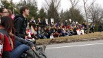 Anti-protestors at the front of the police-lined boundary sit down. The reactions of the students vary, some are angry, others stoic, while others are laughing. Photo by Tim Smith.