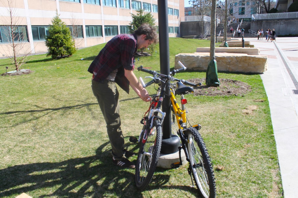 Third-year digital media production major Jared Loperfido locks up his bike outside the Coykendale Science Building before a Milestones in Documentary class. He rides his bike to class from his off-campus apartment about five minutes away. Many students at SUNY New Paltz use bikes as a fast, cheap and eco-friendly way to get around campus and around town. Photo by Faith Gimzek.