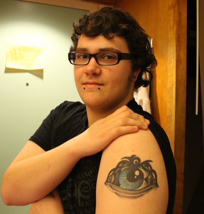 Adams shows off his first tattoo, which symbolizes his transition. The tribal pattern on the top is a replica of the design on a ring his grandmother gave him when he first told her about wanting to change his gender identity. The round shape on the left side of the eye represents being female, while the diamond shape on the right side represents being male. Photo by Faith Gimzek.